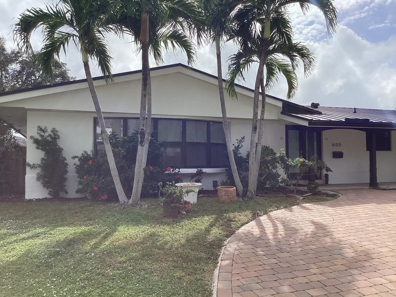 Boca Raton ranch home repainted white with dark window frames behind palms and a paver drive