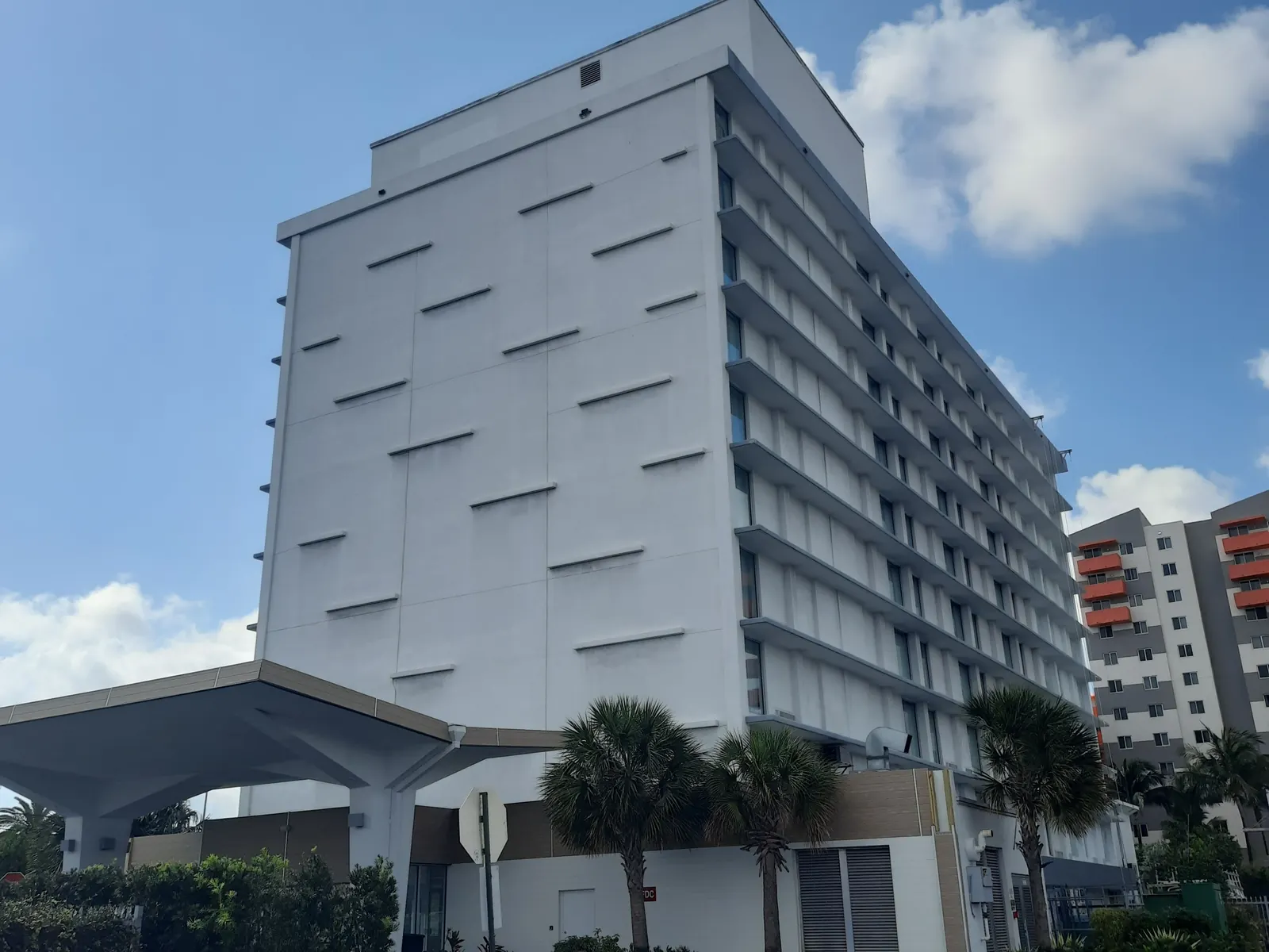 Miami hotel tower repainted white and gray above a porte-cochere and palms
