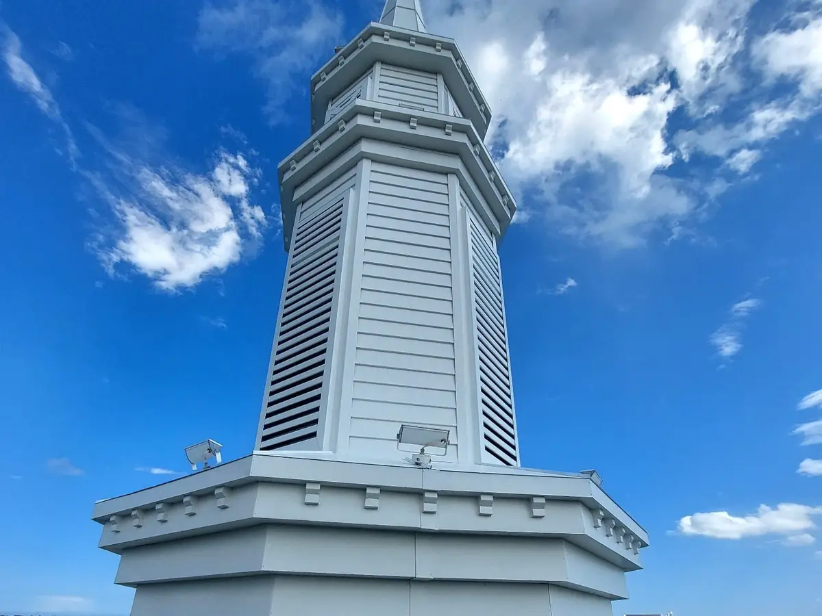 White louvered church steeple after repainting, seen from the roof against a blue sky
