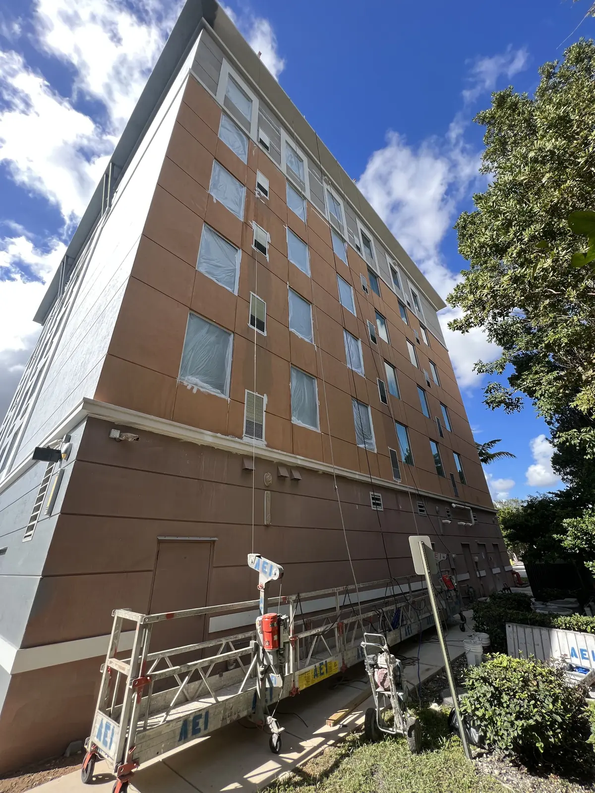 Swing stage rigged against a six-story hotel partway through its repaint