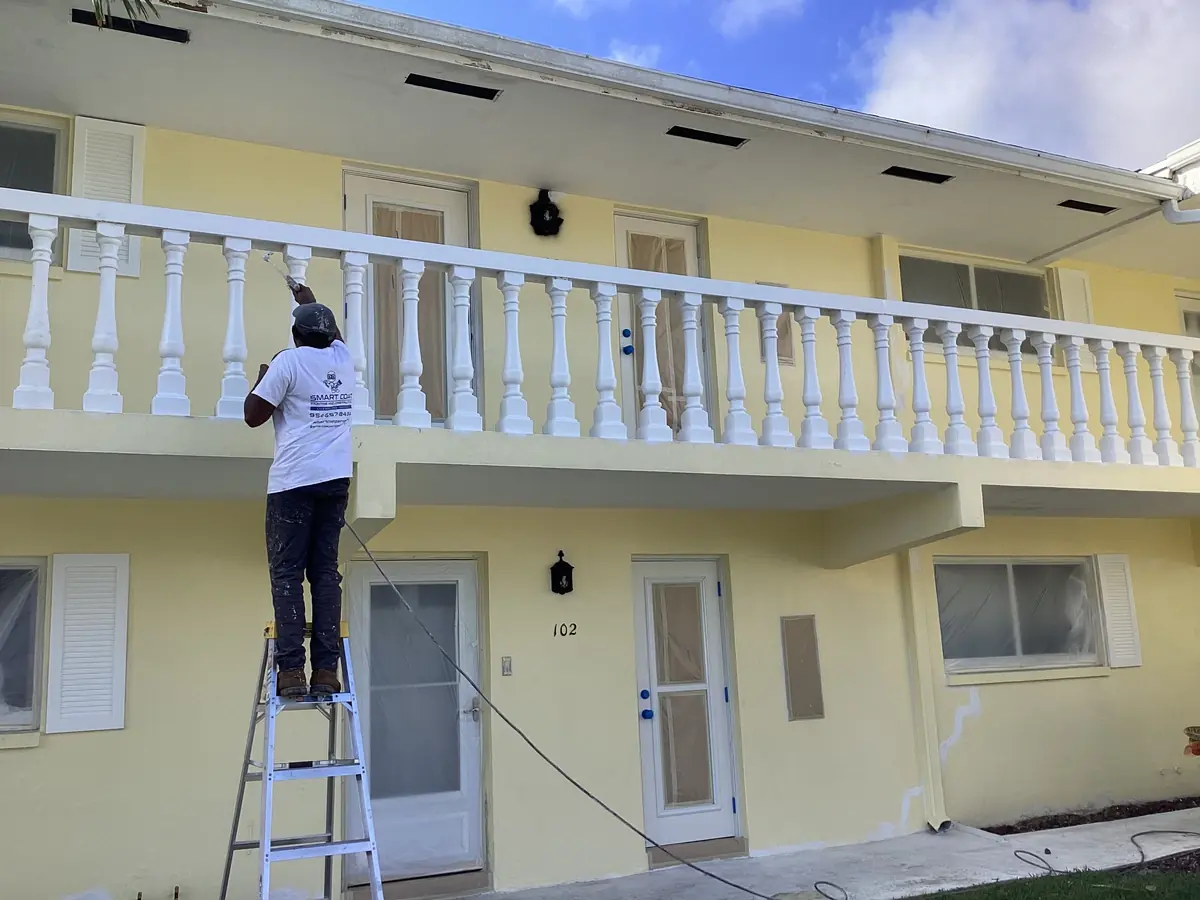 Smart Coat painter on a ladder painting the white balustrade of a garden apartment