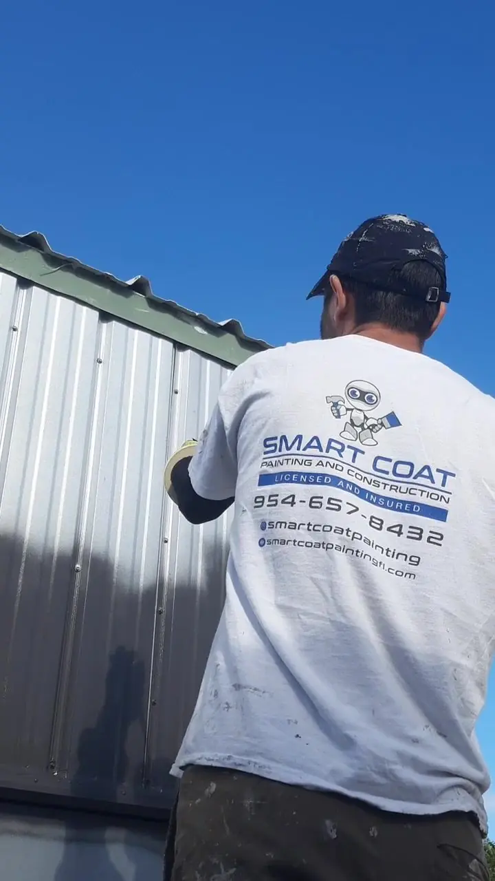 Smart Coat painter in a company shirt working on a metal building's siding
