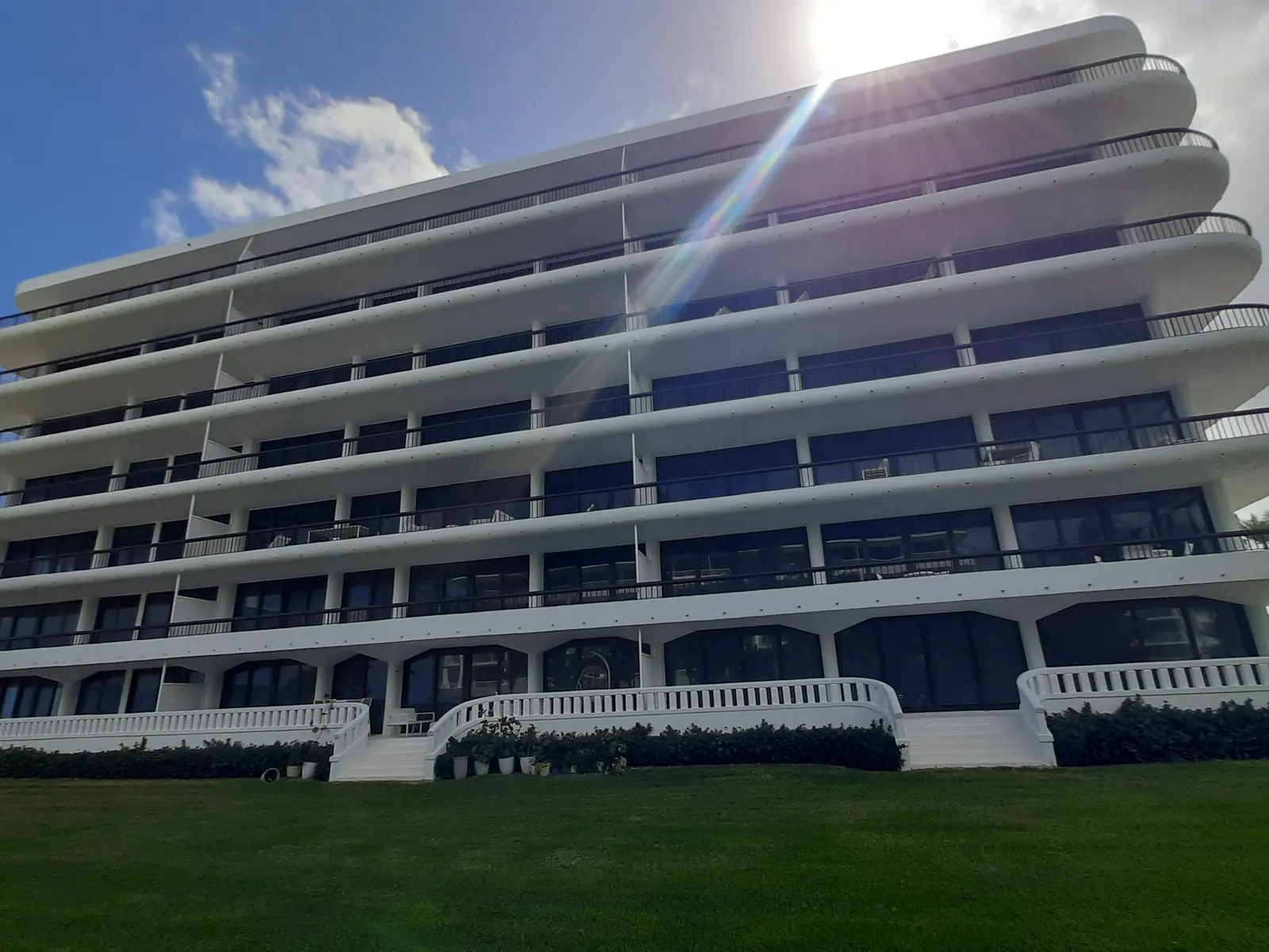 Curved white mid-rise condominium with deep balconies above a lawn