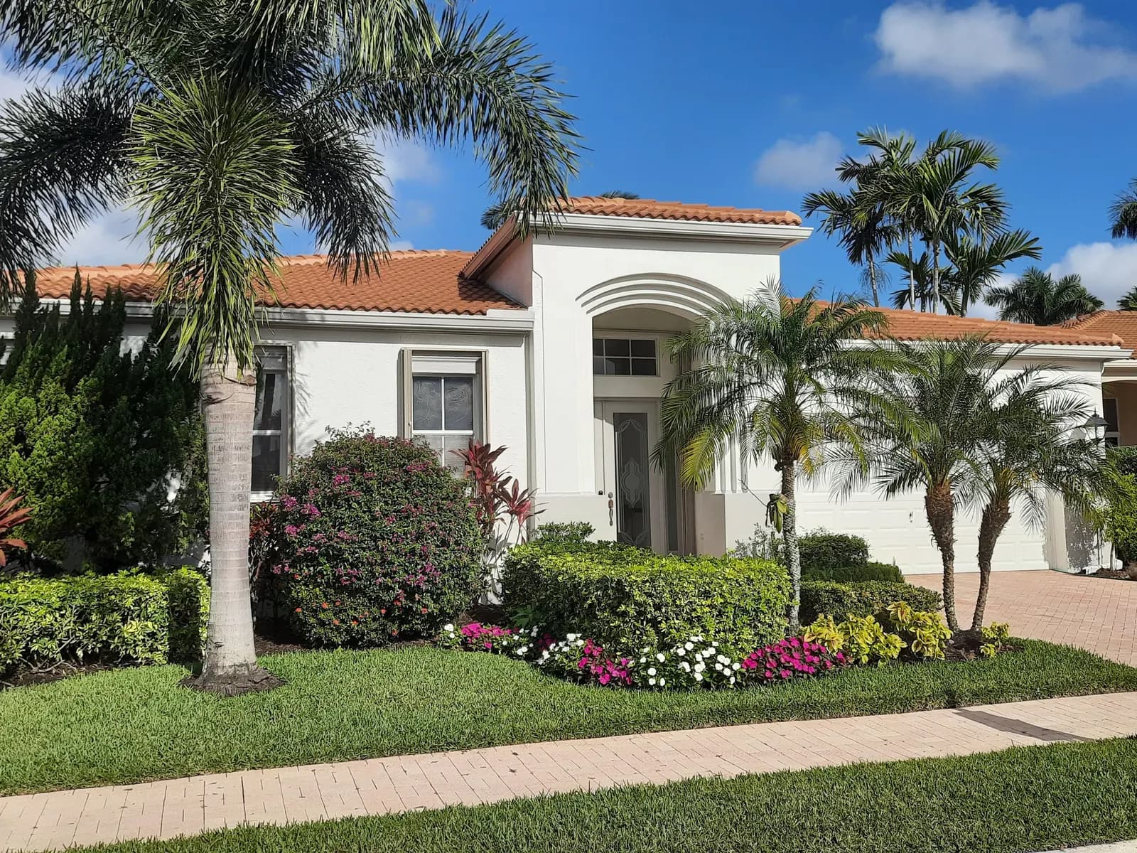 Mediterranean-style home with white stucco, a barrel-tile roof and tropical landscaping