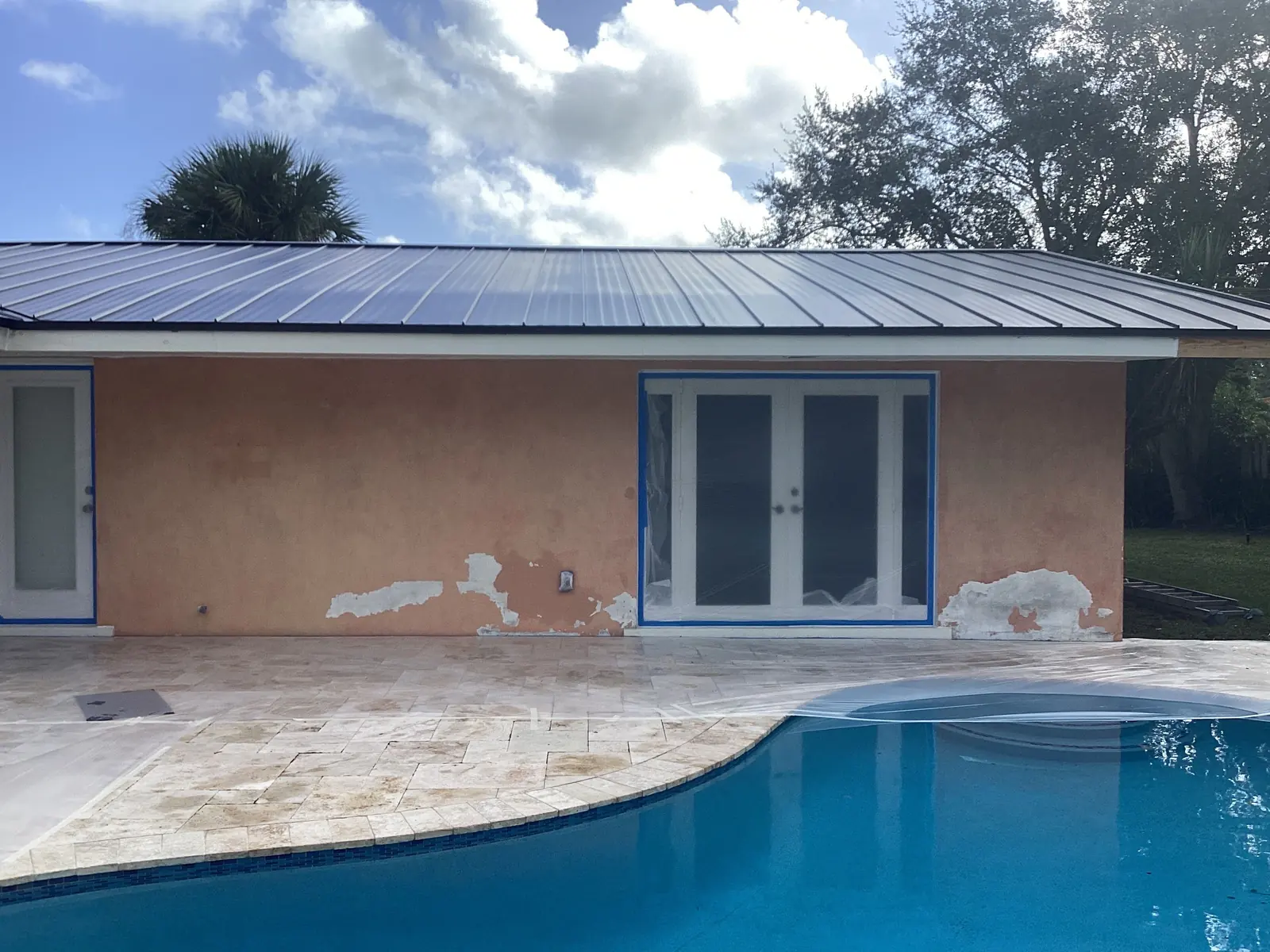Pool house in Boca Raton before work: peeling peach stucco with bare patches below the doors