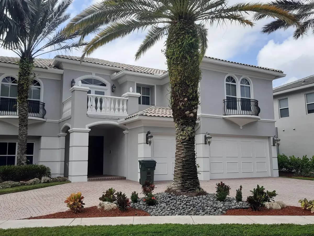 Two-story Mediterranean-style home repainted light gray with white trim behind palms