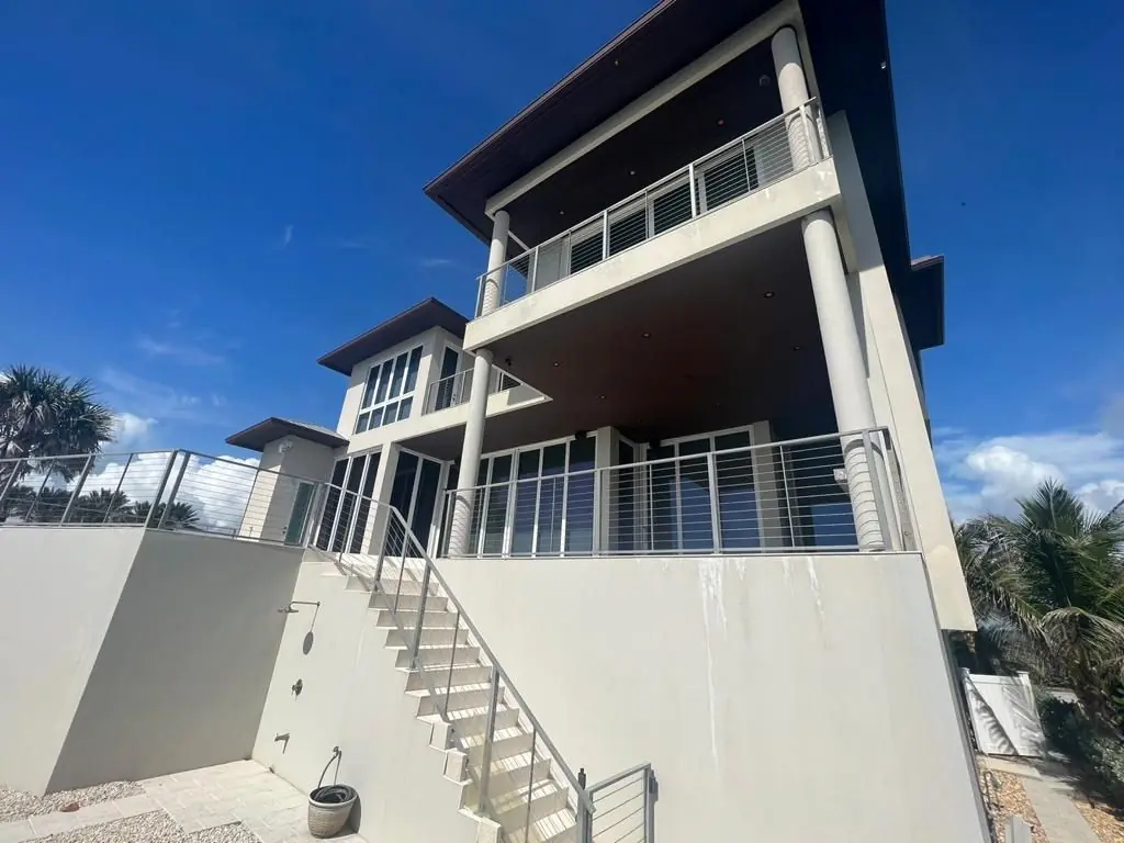 Three-story modern coastal home with white stucco walls and cable railings