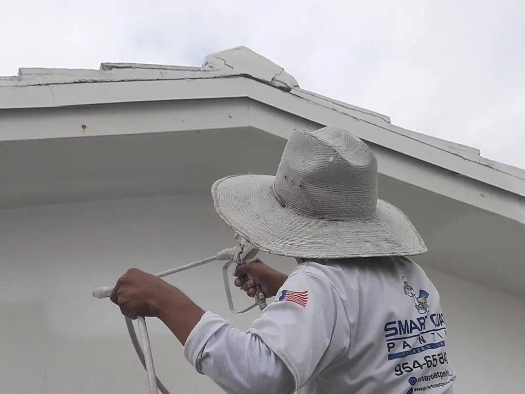 Painter spraying the fascia of a white stucco home from below