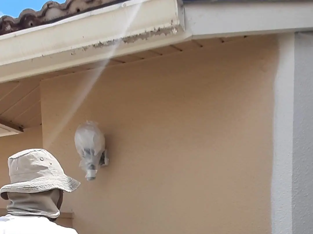 Painter rolling peach paint onto a stucco wall beside a window