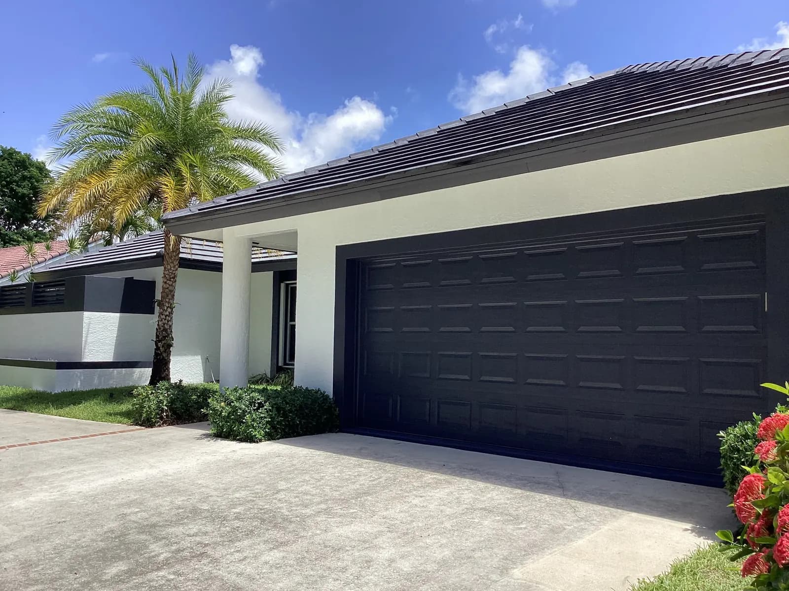 West Palm Beach home repainted white with a black garage door and a dark tile roof beside a palm