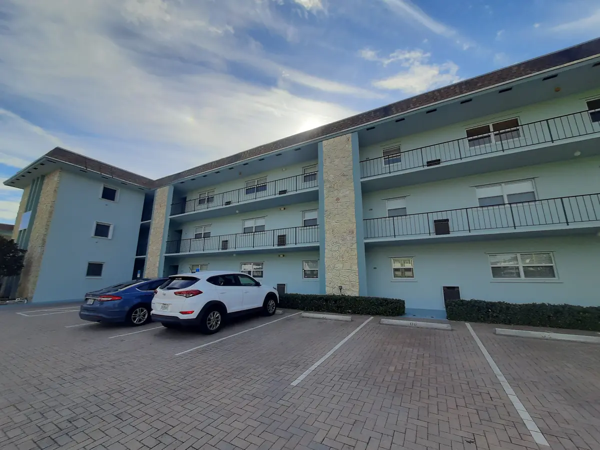 Three-story condominium repainted seafoam green with white railings over a brick parking lot