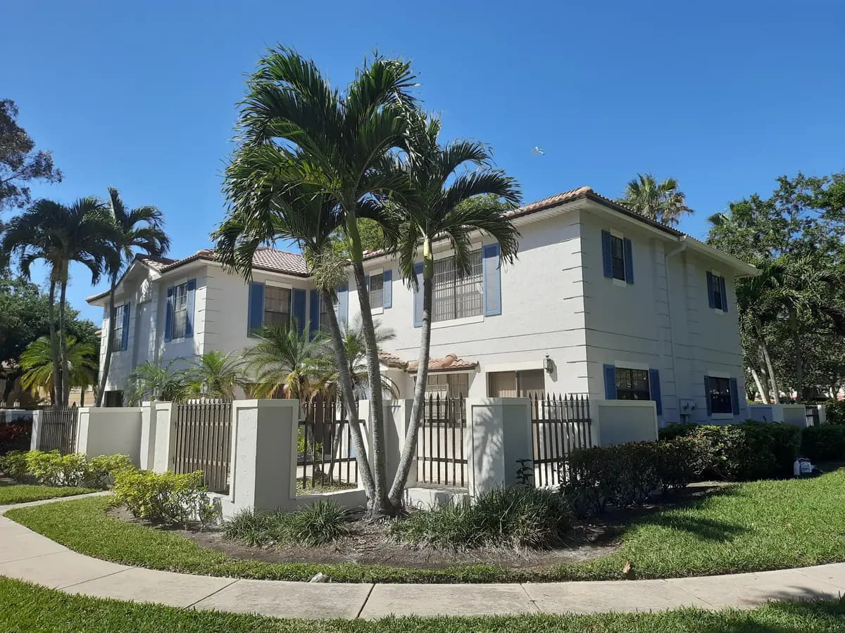 Palm Beach townhomes repainted white with blue shutters behind a garden wall