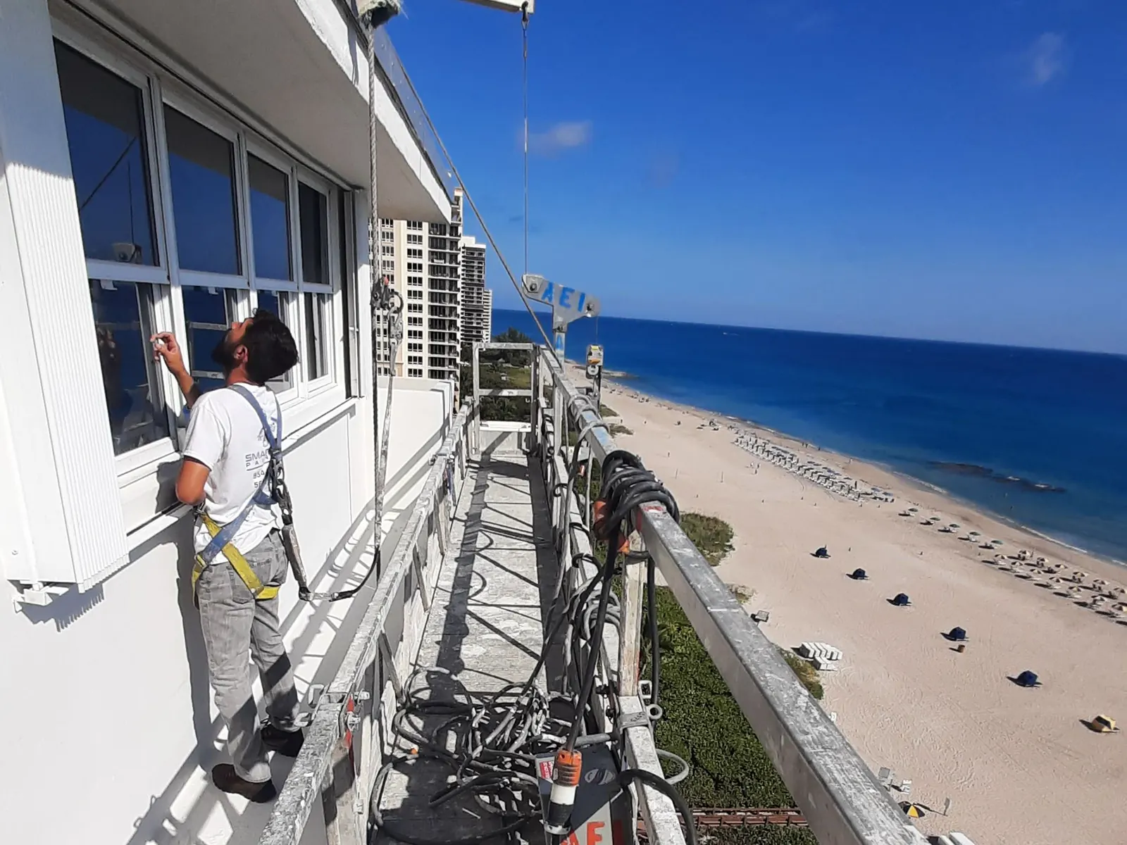 Painter on a swing stage repainting a high-rise facade above the beach