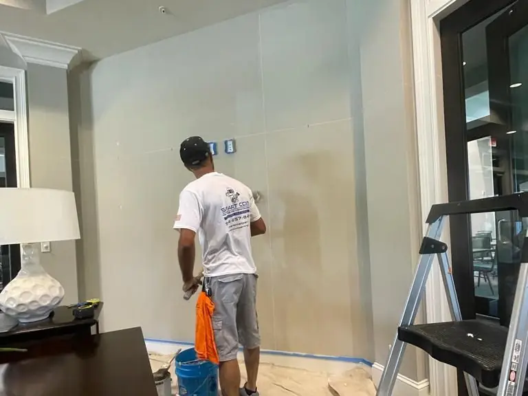 Smart Coat painter rolling a living-room wall over drop cloths, the trim masked