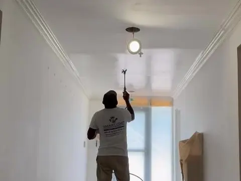 Smart Coat painter spraying a hallway ceiling, the floor covered and taped