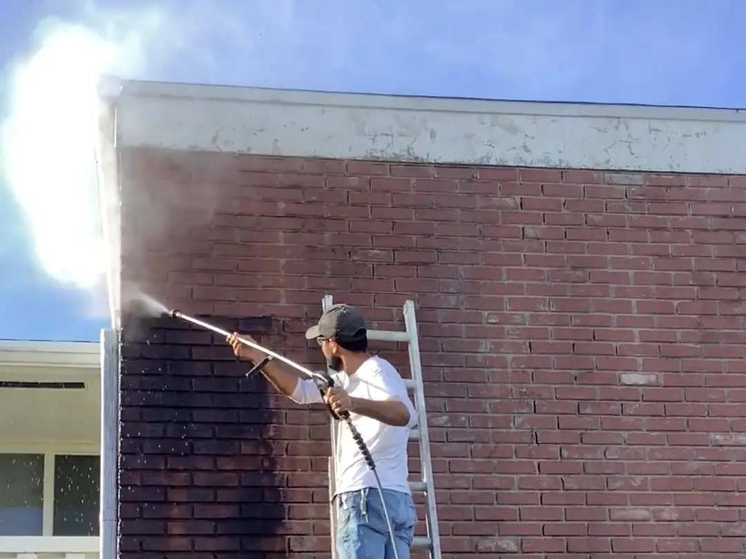Worker on a ladder pressure washing a brick chimney