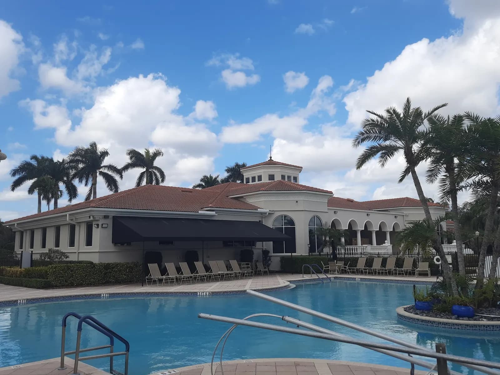 Clubhouse with a clean terracotta tile roof after Roof-A-Cide, a pool and royal palms in front