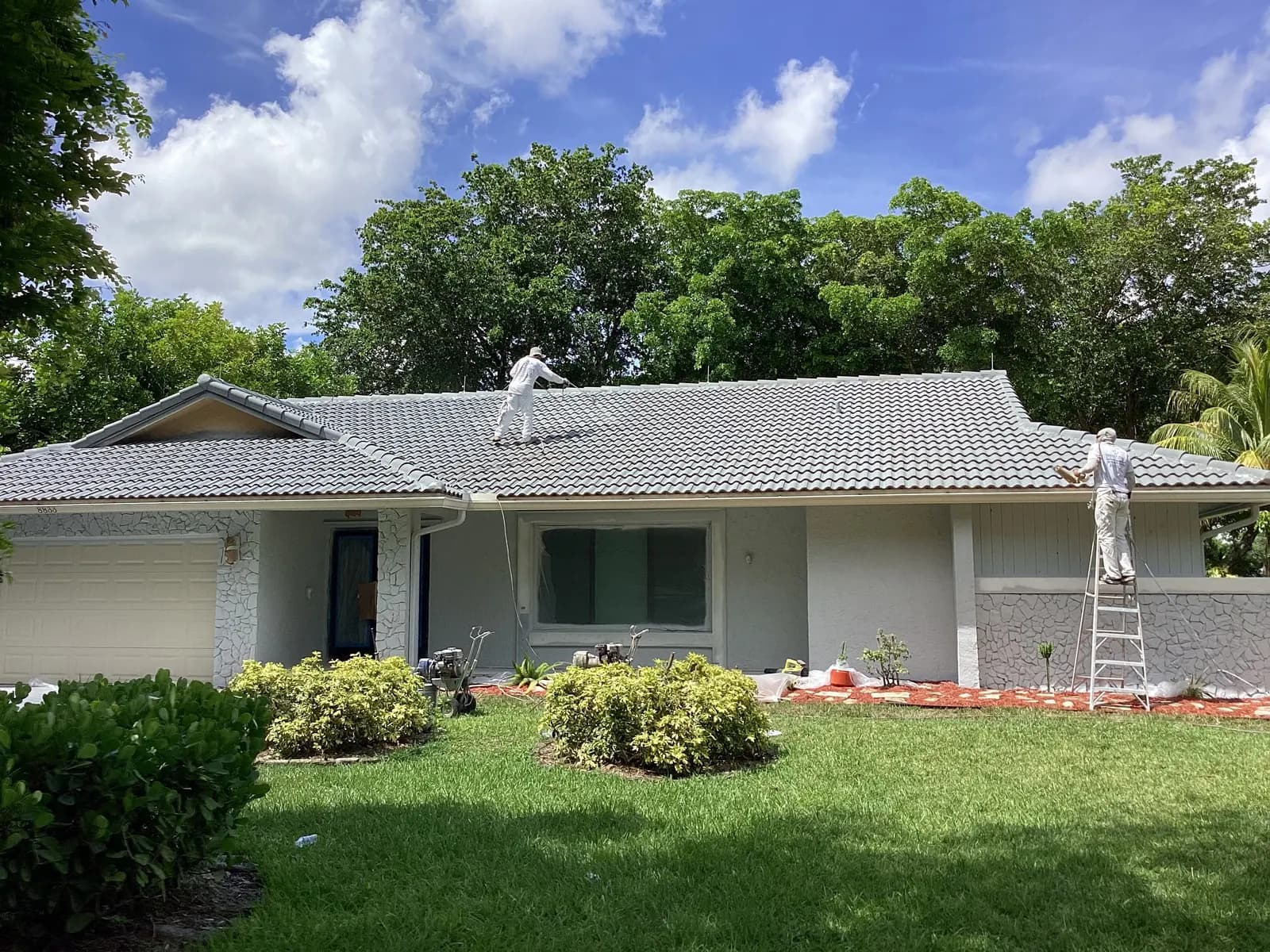 Two painters spraying a gray roof coating on a Coral Springs home, one on the roof, one on a ladder