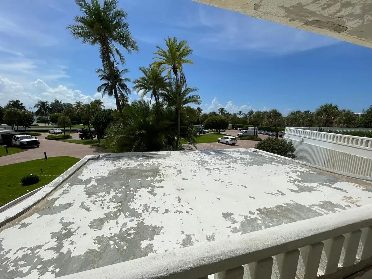 Worn flat roof with peeling coating before restoration, palms behind