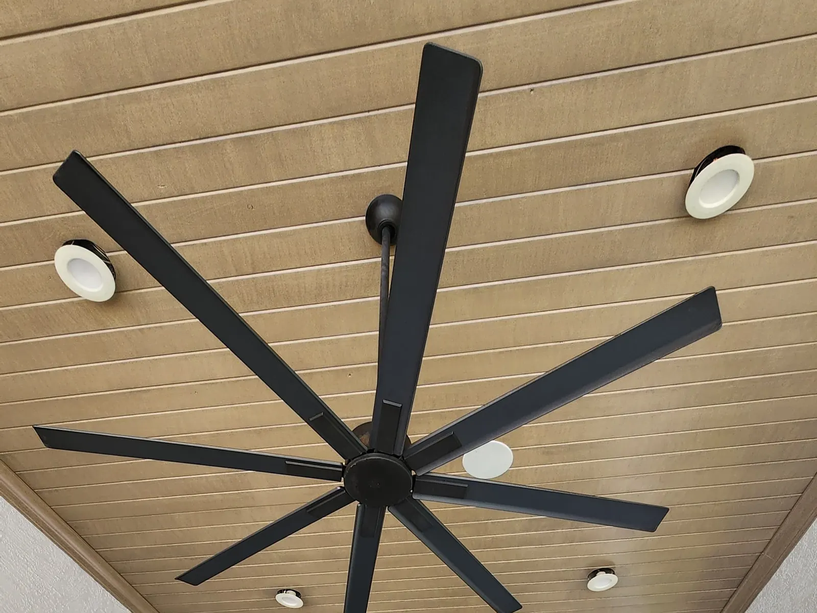 Covered patio with a faux wood-grain ceiling finish and black ceiling fans beside a pool