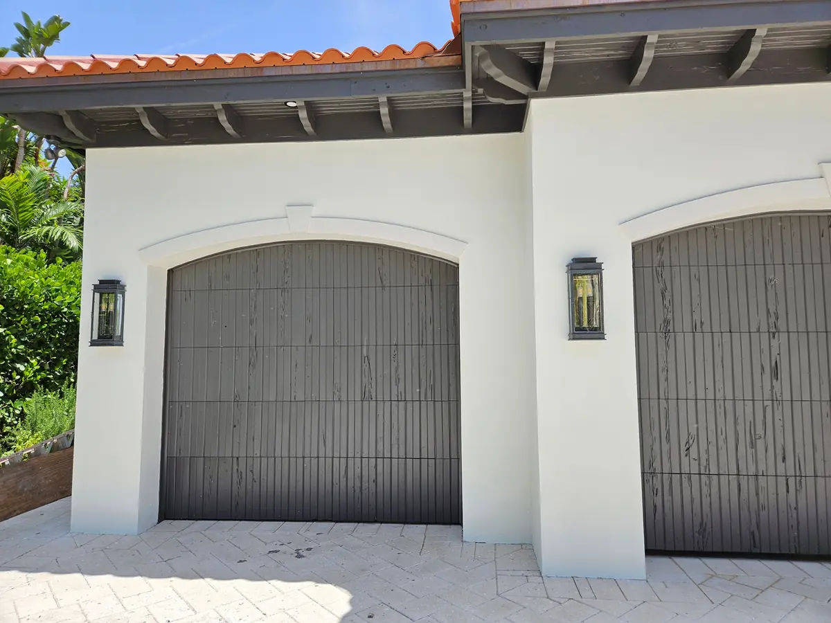 Arched garage doors in Jupiter finished in a weathered wood look under a tile roof