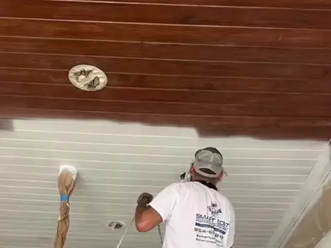 Painter on a scaffold applying a faux wood-grain finish to a patio ceiling