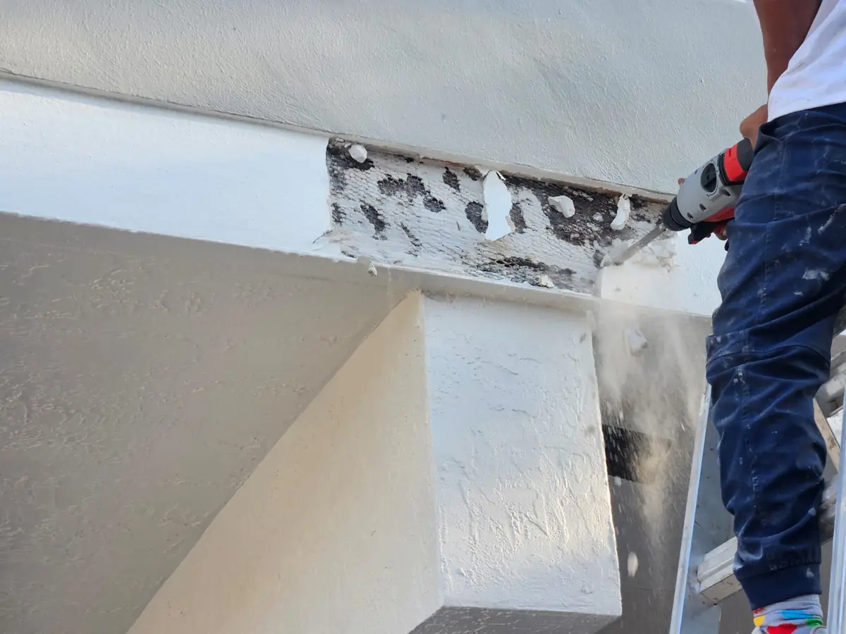 Worker grinding out damaged stucco on a beam before patching