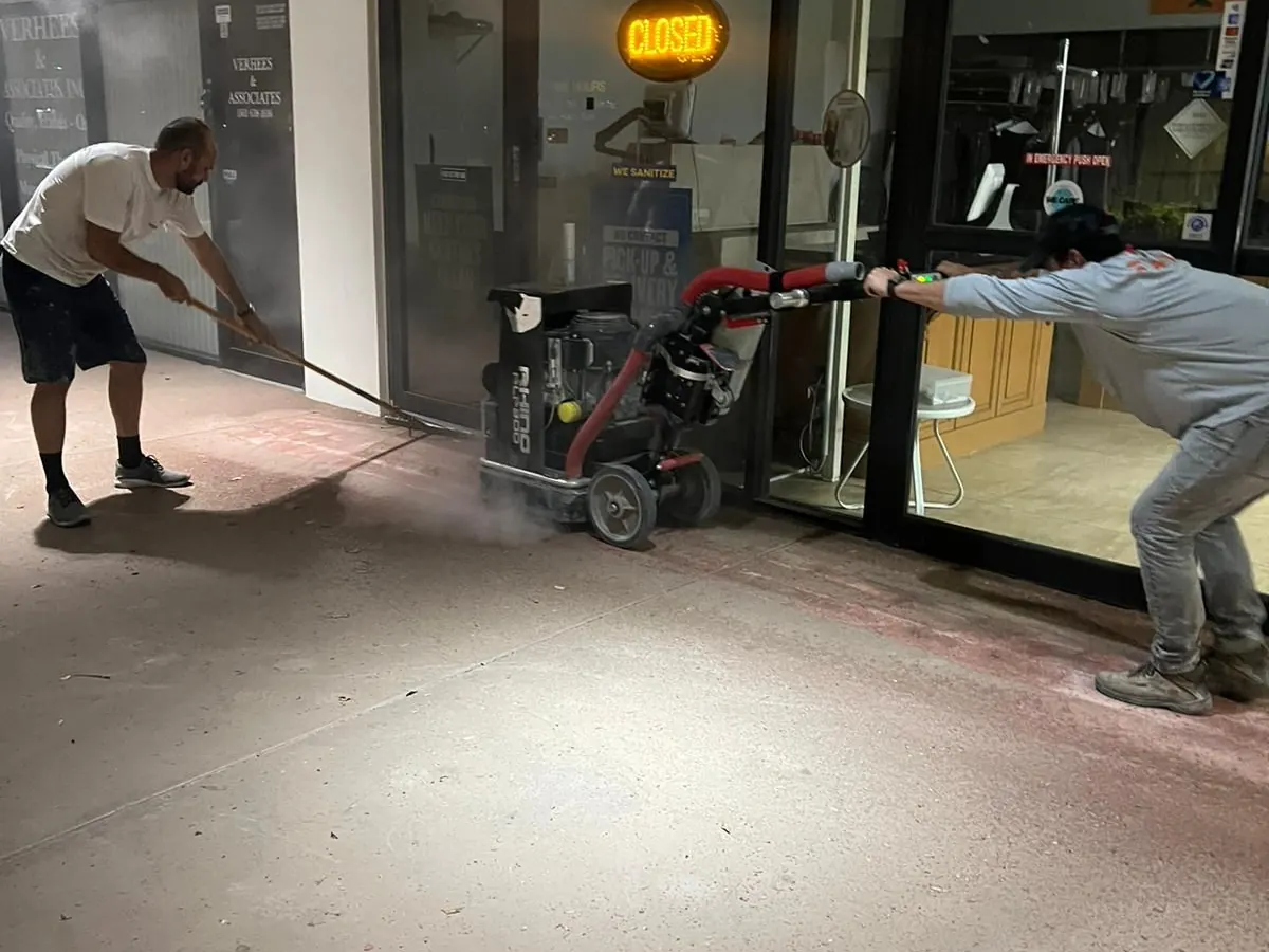 Two workers diamond-grinding a concrete floor at a storefront