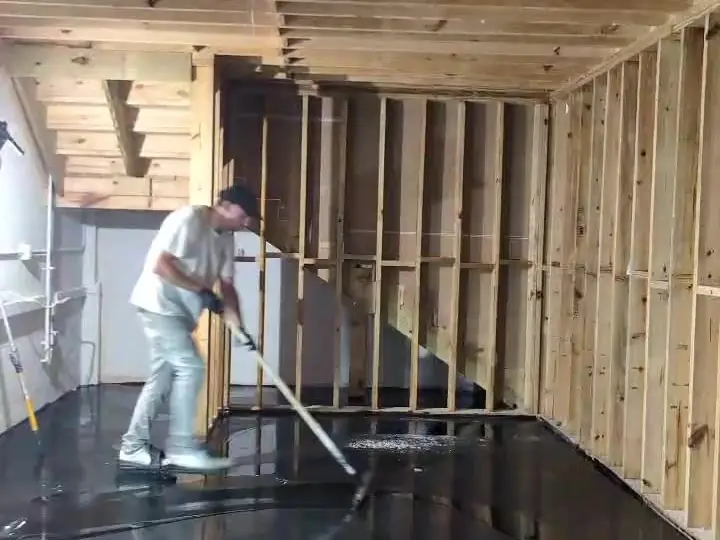 Worker rolling black epoxy onto a prepared floor under open framing