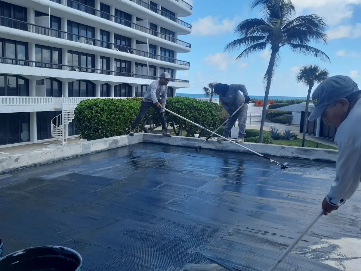 Two workers spreading membrane across a plaza deck, buckets of coating in front